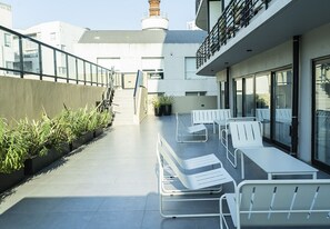 A rooftop terrace with white lounge chairs, a concrete pathway, and a view of surrounding buildings. - San Telmo: Modern, with Premium Amenities, Strategic Connection (Buenos Aires)