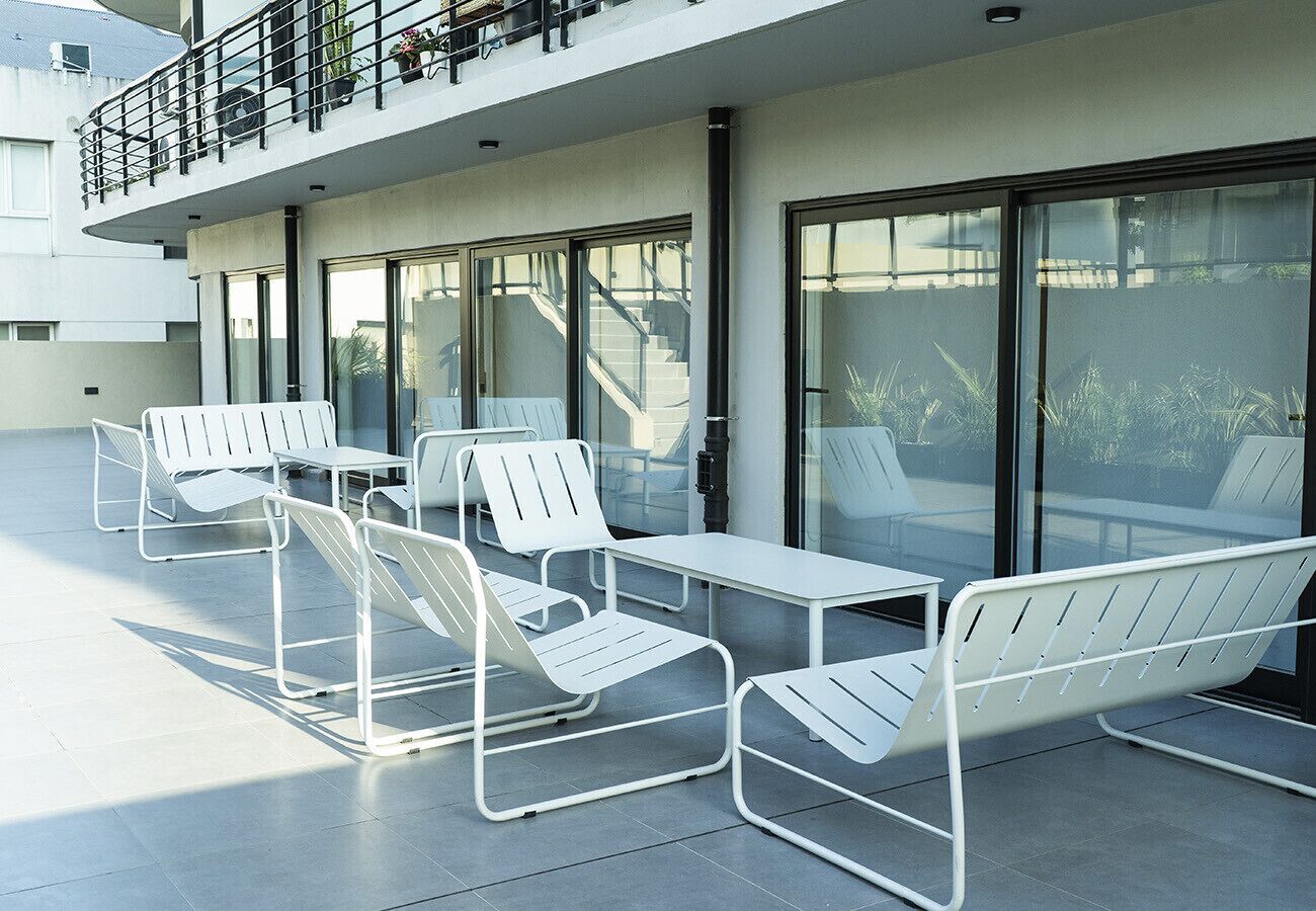 A modern outdoor seating area with metal chairs and tables, a balcony with a railing, and a building with large windows.