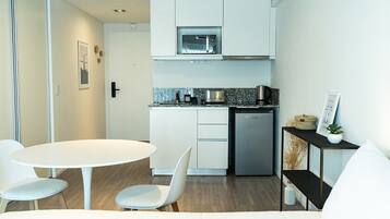 A compact kitchen with white cabinetry, a microwave, and a coffee machine. There is a small dining area with a white table and chairs.