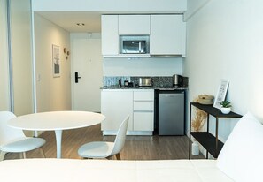A compact kitchen with white cabinetry, a microwave, and a coffee machine. There is a small dining area with a white table and chairs. - San Telmo: Modern, with Premium Amenities, Strategic Connection (Buenos Aires)