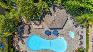 Luftaufnahme eines Poolbereichs mit Liegestühlen, Sonnenschirmen und einem Whirlpool.