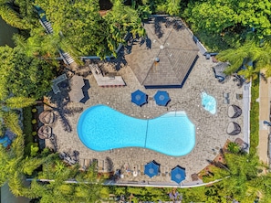 An aerial view of a swimming pool area with lounge chairs, umbrellas, and a hot tub.