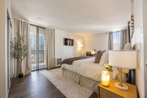 Ein modernes Hotelzimmer mit einem großen Bett, einer Nachttischlampe, einem Fernseher und Blick auf die Stadt.