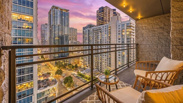 Ein Balkon mit Korbmöbeln, einem kleinen Tisch mit einer Pflanze und Blick auf die Stadt im Abenddämmerung.