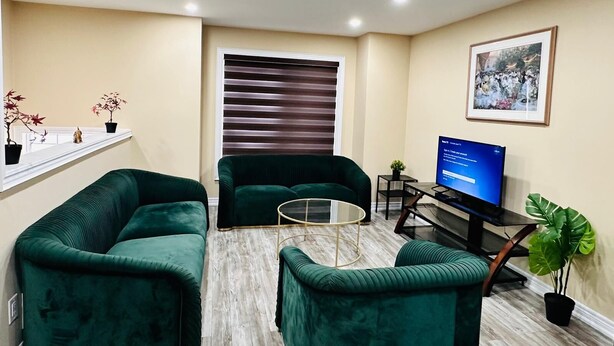 Ein Wohnzimmer mit zwei grünen Sofas, einem Glastisch, einem Fernseher und einem gerahmten Bild an der Wand.