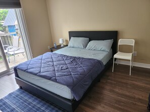 Un dormitorio con cama, mesita de noche, silla y vistas al exterior.