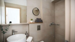 Ein Badezimmer mit großem Spiegel, Waschbecken, Dusche und Ablagefläche mit Handtüchern und einer Pflanze.