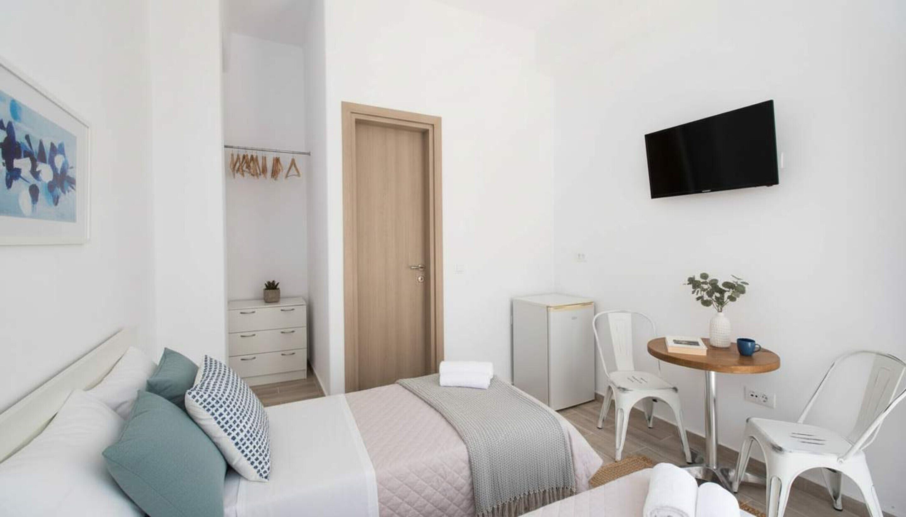 A modern hotel room with a bed, a desk with a chair, a TV, and a small table with a plant.
