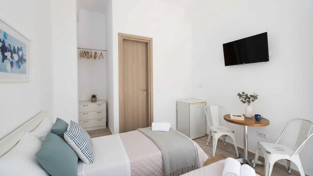 Ein modernes Hotelzimmer mit Bett, Schreibtisch mit Stuhl, Fernseher und einem kleinen Tisch mit Pflanze.