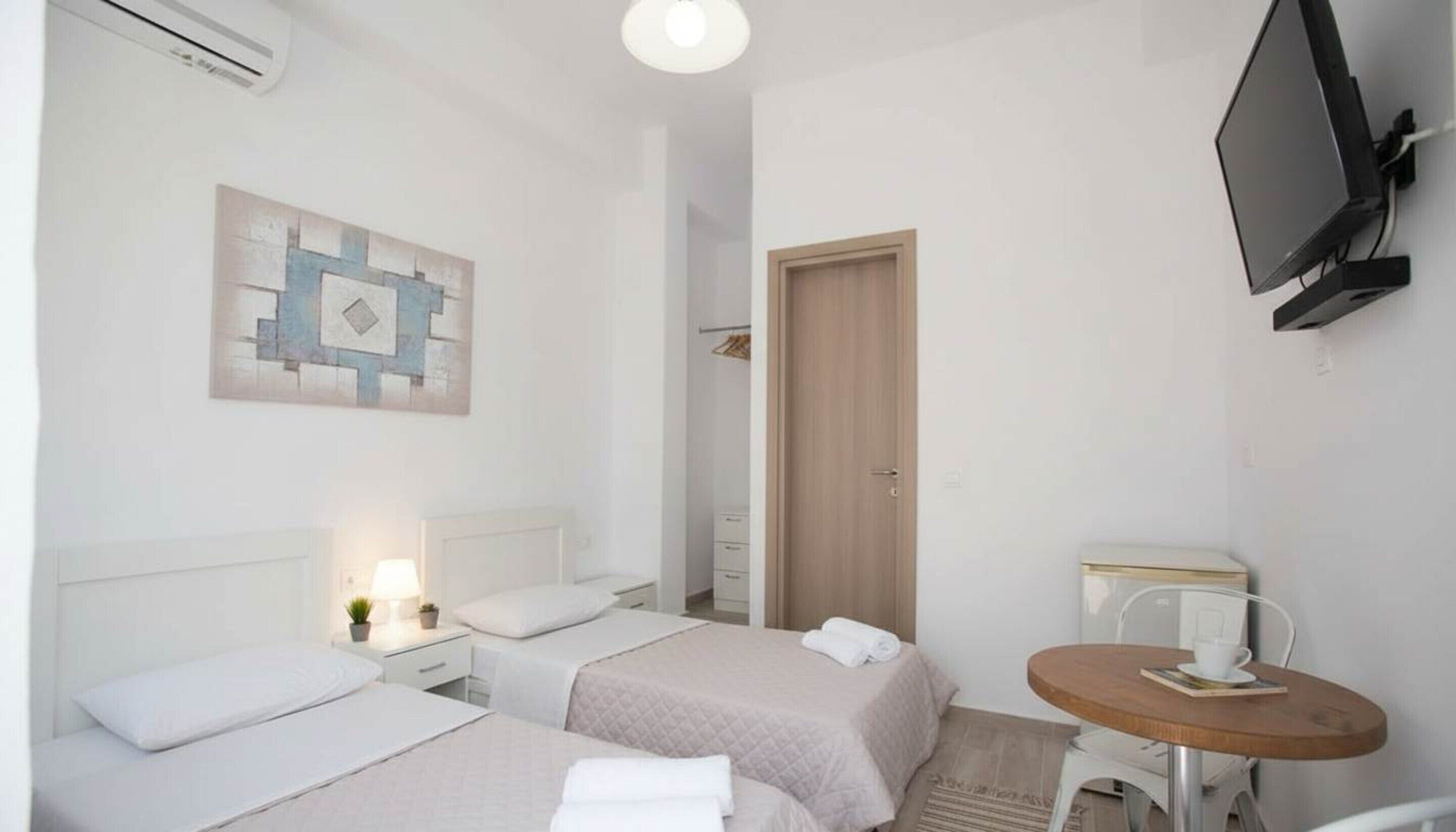 Ein Hotelzimmer mit zwei Betten, einem Fernseher, einem kleinen Tisch und einem Bild an der Wand.