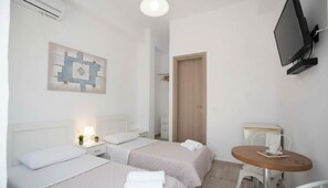 Ein Hotelzimmer mit zwei Betten, einem Fernseher, einem kleinen Tisch und einem Bild an der Wand.