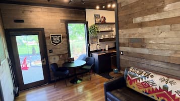 A modern interior with a wooden wall, a sofa, a dining area with chairs, and a kitchen area with a sink and shelves.