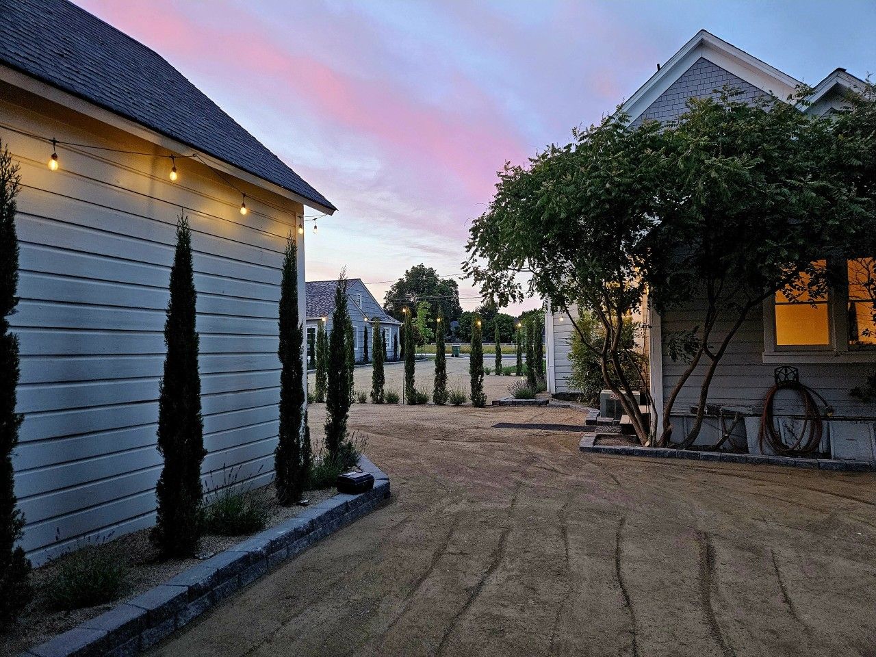 A residential driveway with a gravel surface, bordered by a low curb, and houses on either side.