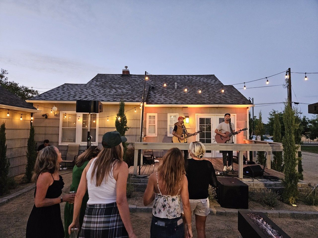 An outdoor patio area with a stage for live music, surrounded by guests.