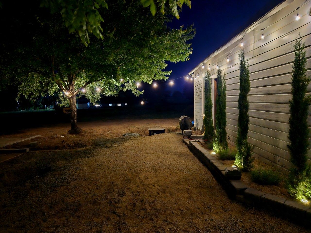 Une allée de gravier menant à un bâtiment décoré de guirlandes lumineuses et bordé d’un arbre.