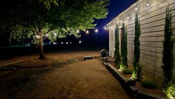 Une allée de gravier menant à un bâtiment décoré de guirlandes lumineuses et bordé d’un arbre.
