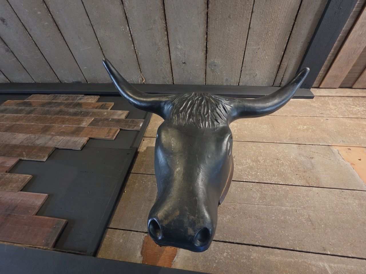 Une sculpture représentant une tête de taureau, posée sur un sol en béton, avec des planches de bois et une rambarde métallique en arrière-plan.
