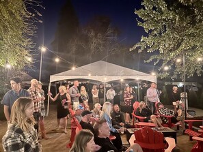 A group of people gathered around a tent with string lights, seated on red chairs, and standing under a canopy. - Villa Brut- Built in 1902 to hold ice. Now it holds guests. (Dundee)