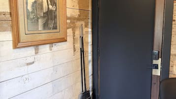 A room with a wooden wall, a framed picture, a door, a doormat, and a chair.
