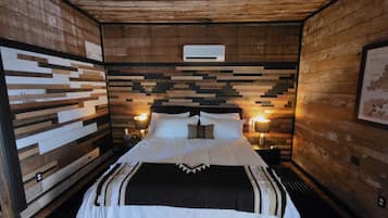 A room with a bed, wooden walls, and two wall-mounted lamps.