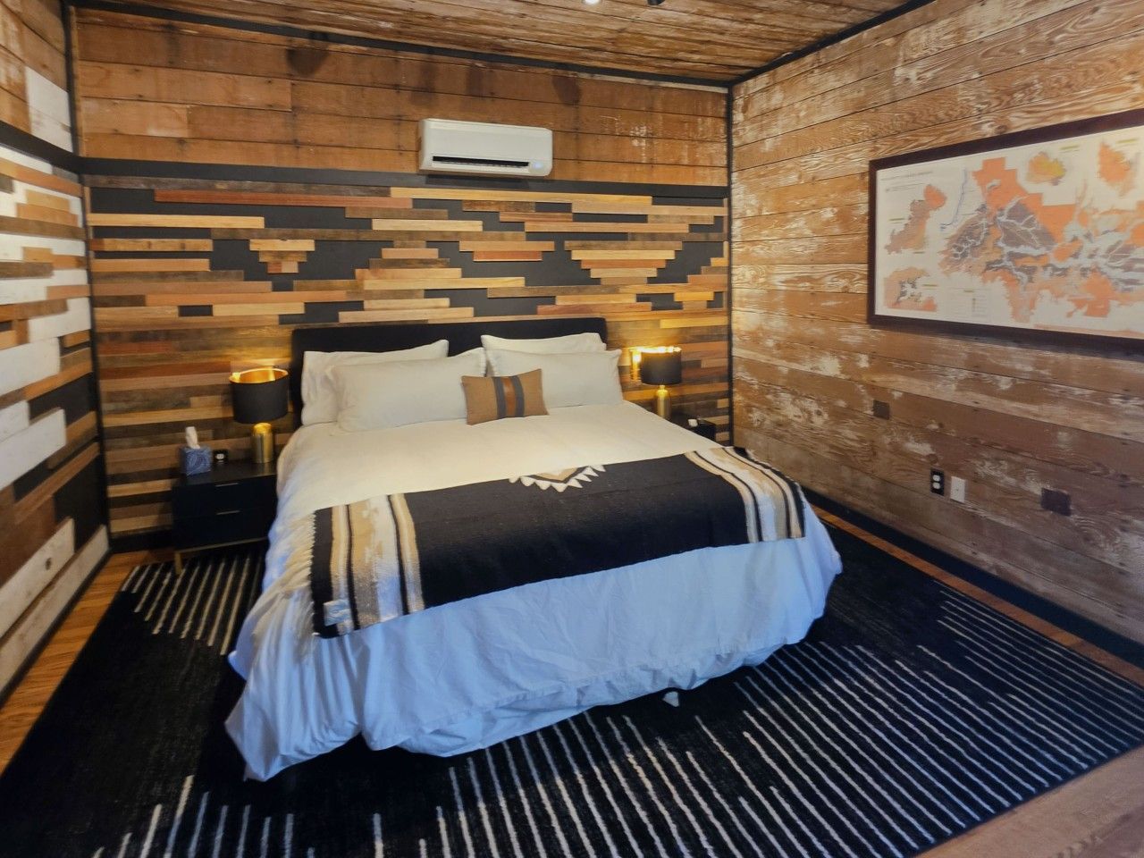 Une chambre comprenant un lit, une table de chevet, un climatiseur fixé au mur et une carte encadrée accrochée au mur.