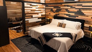 A bedroom with a bed, a wooden wall panel, a black-framed door, and an air conditioning unit.