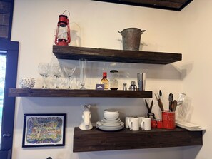 Een keuken met houten planken waarop drinkglazen, een lantaarn en keukengerei staan.