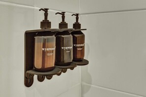 A bathroom with a wall-mounted shelf holding four bottles of Wynywood products. - w* | Amazing Loft in the Heart of Chico Norte (Bogotá)