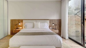 Een moderne slaapkamer met een groot bed, een houten hoofdbord, twee nachtkastjes met lampen, en een schuifglazen deur aan de rechterkant.