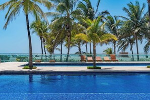 A pool area with palm trees, lounge chairs, and a clear view of the ocean. - w* | Deluxe 2BR w/ Terrace & A/C in Morros (Cartagena de Indias)