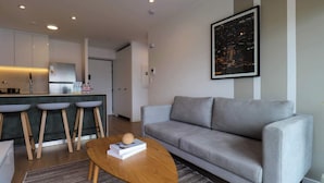 A modern living room with a grey sofa, a wooden coffee table, and a kitchen area with a bar and stools. - w* | Cityview 2BR w/ Balcony in Miraflores (Miraflores)
