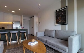 A modern living room with a grey sofa, a wooden coffee table, and a kitchen area with a bar and stools. - w* | Cityview 2BR w/ Balcony in Miraflores (Miraflores)