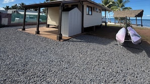Un edificio frente a la playa con un porche cubierto, un garaje y una estructura con techo de paja.