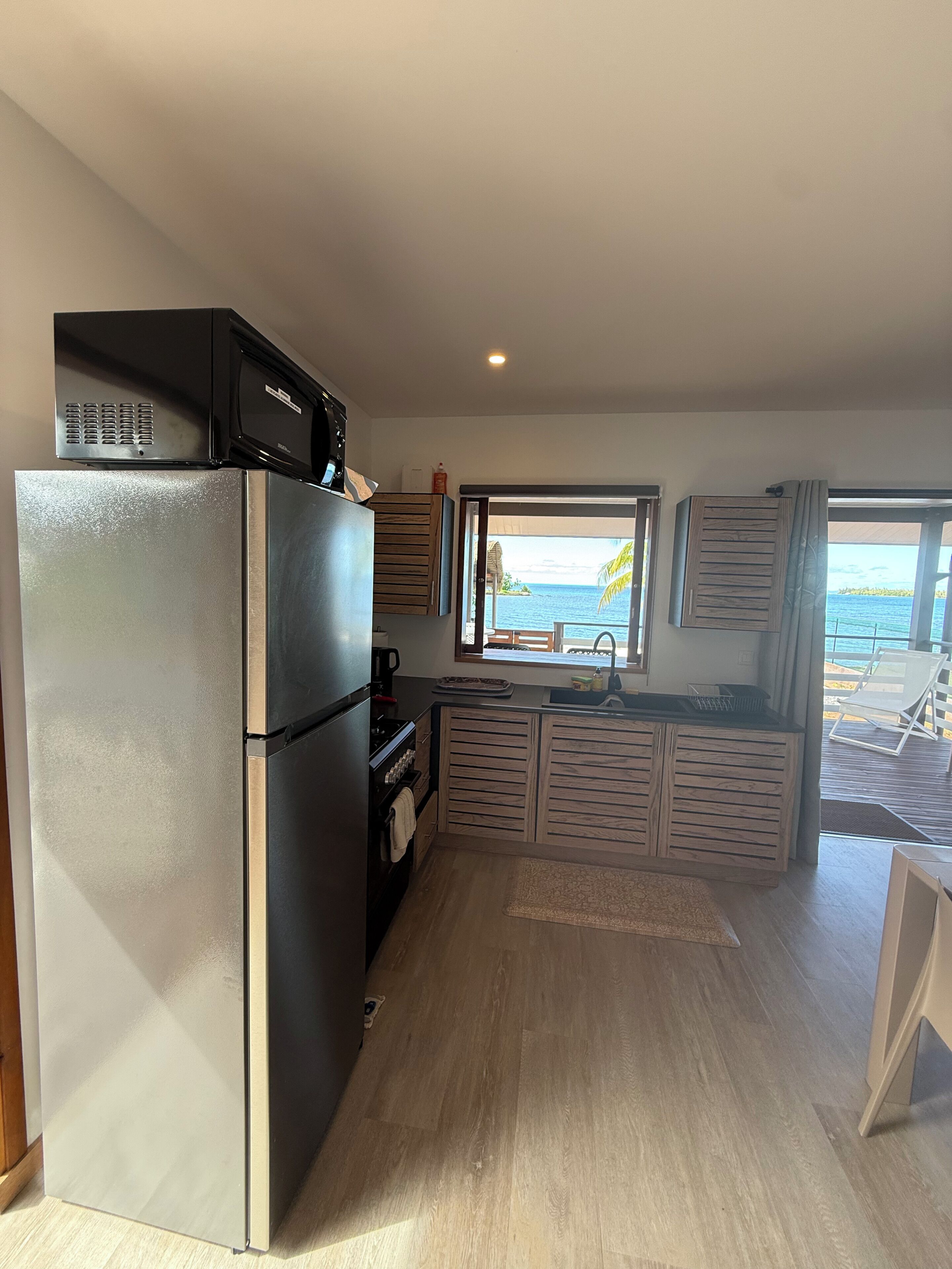 Cocina compacta con refrigerador, horno y microondas. Cuenta con un amplio ventanal con vista al mar y un balcón con una silla.