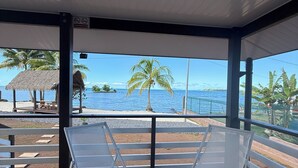 A covered outdoor area with two white lounge chairs, a thatched-roof structure, and a view of the ocean. - Le TeRava (Raiatea)