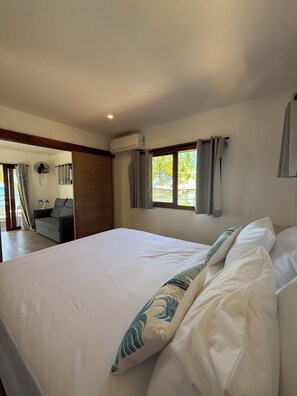 A bedroom with a large bed, a ceiling fan, an air conditioning unit, and a view of the outdoors. - Le TeRava (Raiatea)