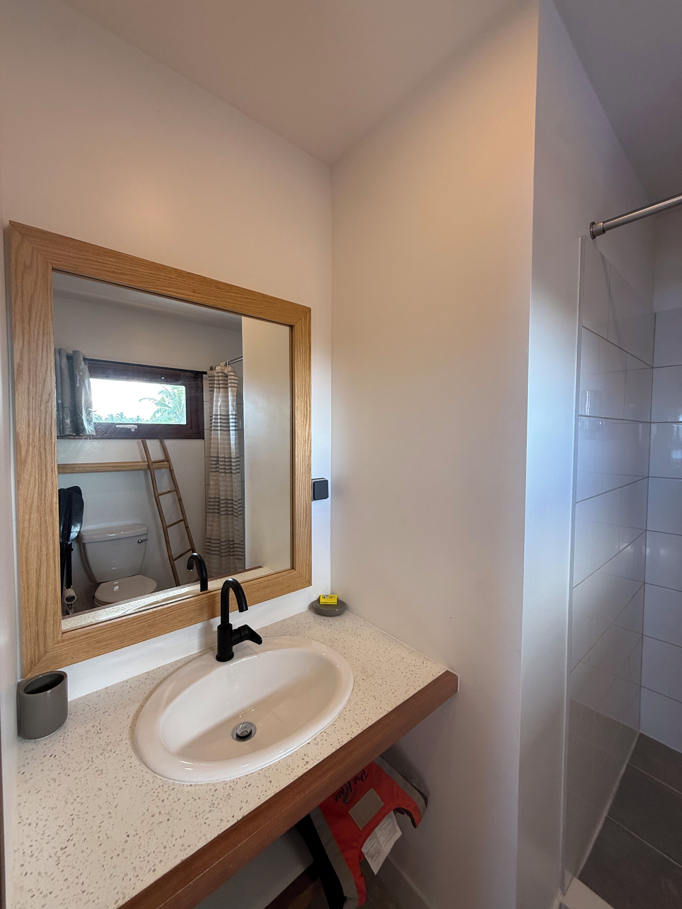 A bathroom with a white sink, a wooden-framed mirror, and a shower area.