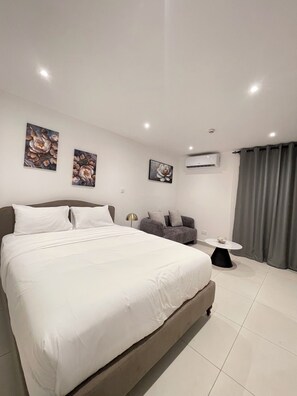 A modern hotel room with a large bed, a sofa, a small table, and artwork on the walls. - Delali Residence Luxury 1BR Near Airport, Pool, Gym & private Terrace (Accra)