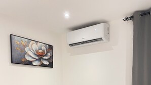 A modern living room with a grey sofa, a round black table, and a wall-mounted air conditioner. - Delali Residence Luxury 1BR Near Airport, Pool, Gym & private Terrace (Accra)