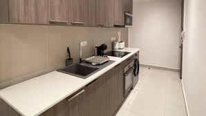 A modern kitchen with wooden cabinets, a white countertop, a built-in oven, and a microwave. - Delali Residence Luxury 1BR Near Airport, Pool, Gym & private Terrace (Accra)