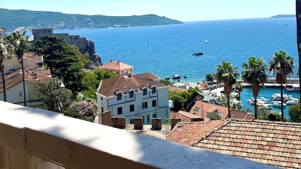 Uma vila costeira com vista para o mar, edifícios com telhados vermelhos e céu claro.