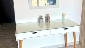 Um console branco com bancada de vidro, pernas de madeira e um espelho em cima.
