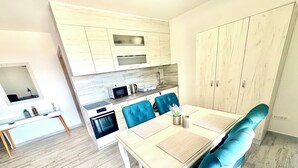 Uma cozinha moderna com armários brancos, micro-ondas e fogão. Há uma área de refeições com mesa e cadeiras azuis.