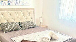Cama bem arrumada com manta marrom, toalha enrolada e almofadas estampadas.