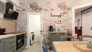 Cozinha compacta com parede de tijolos, área de jantar com mesa e cadeiras, e lavanderia com máquina de lavar.