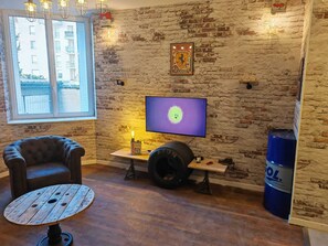 A room with a brick wall, a television, a leather chair, a round wooden table, and a window. - The Atelier Apartment, 4-star rated, sleeps up to 5 people (Metz)