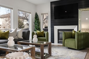 A modern living room with a fireplace, a green armchair, a sofa, and a glass coffee table. - Entire Home•Sleeps 14•Hot Tub•Pool Table•BBQ (Edmonton)