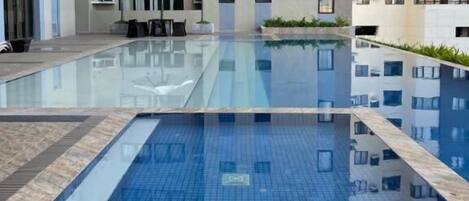 A modern residential building with a swimming pool, air conditioning units, and a covered seating area.
