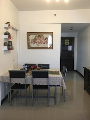 A dining area with a table set for four, chairs, a framed picture on the wall, and a kitchen in the background. - Cozy Room at The Persimmon (Cebu City)