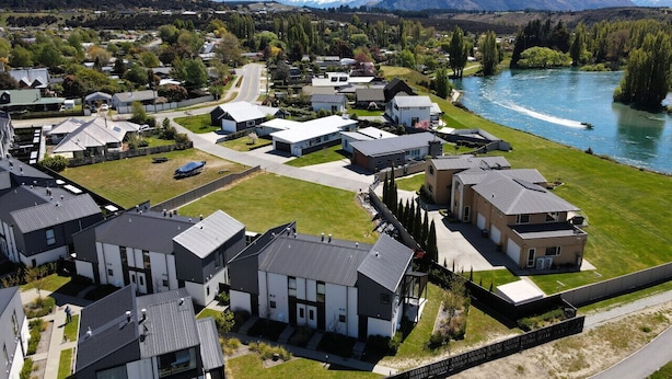 Een woonwijk met moderne huizen, een rivier en bergen op de achtergrond.